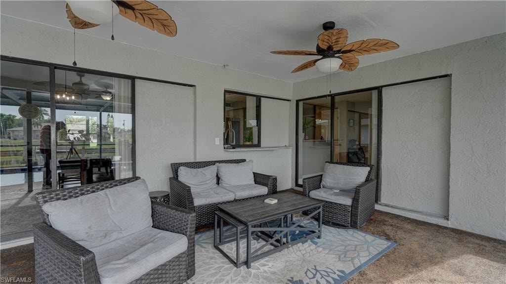 Covered outdoor patio featuring two ceiling fans with decorative blades, textured walls, and multiple sliding glass doors