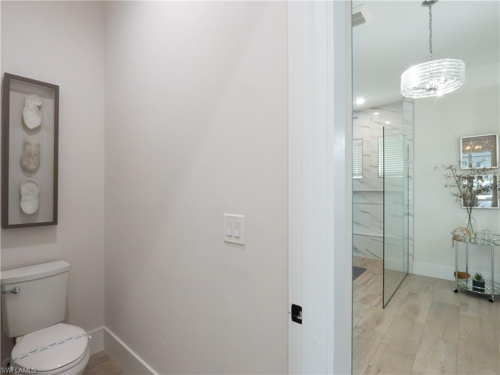 Modern bathroom featuring a frameless glass shower enclosure with wood-finish flooring, white subway tile surround, contemporary pendant lighting, and a separate water closet with ceramic fixtures