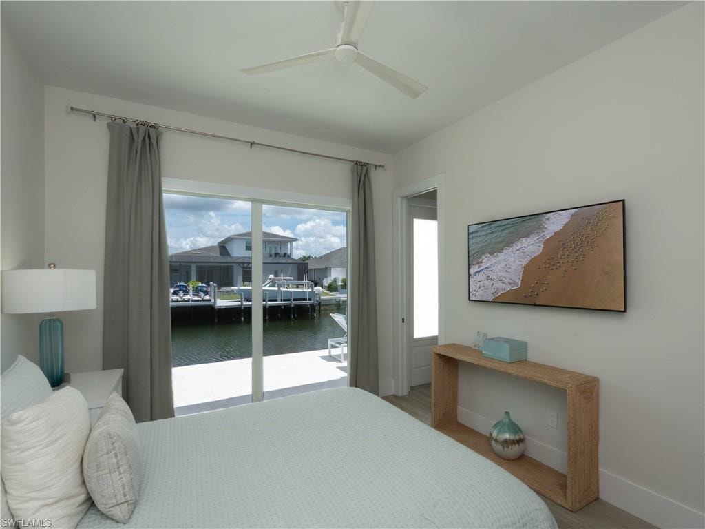 Sliding glass doors opening to waterfront, modern ceiling fan, wall-mounted television, wood-finish flooring