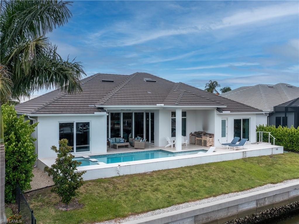 Modern residence featuring a resort-style backyard with sparkling saltwater pool, expansive lanai with sliding glass doors, manicured lawn, mature palm trees, and a gray tile roof with clean architectural lines
