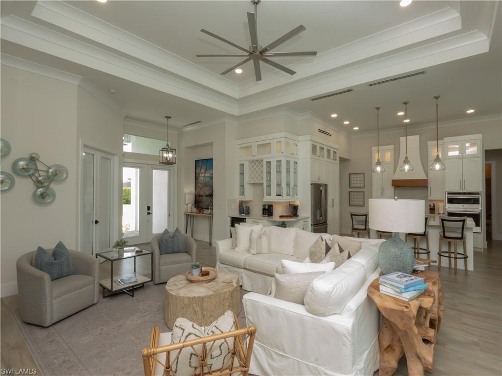Tray ceiling with crown molding, plank-style flooring, white built-in cabinetry, stainless steel appliances, and a large central island with seating