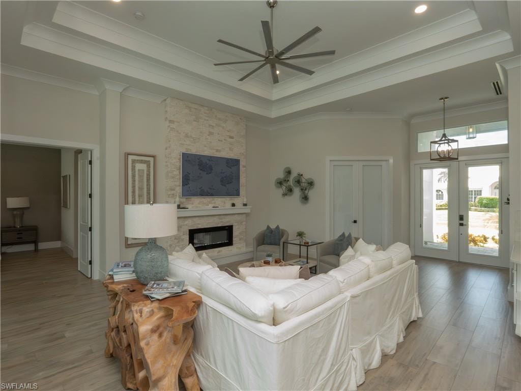 Spacious living area featuring a tray ceiling, wood-finish flooring, a stone-clad fireplace, and double-door entry with transom windows