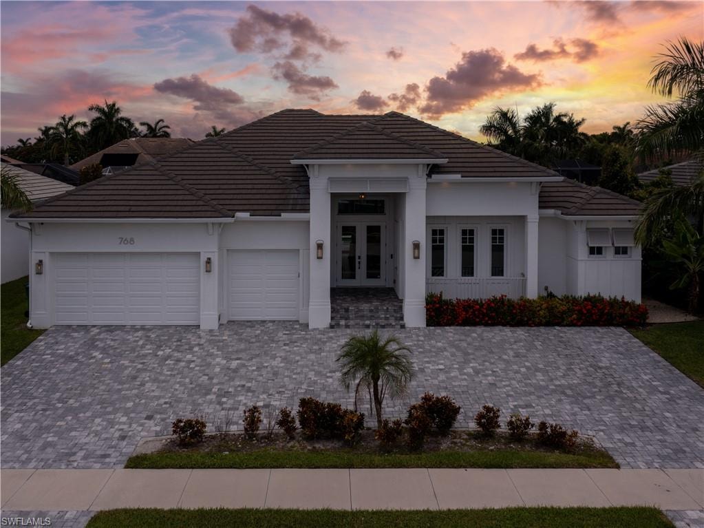 Modern white stucco residence featuring a hipped tile roof, three-car garage with panel doors, and a circular driveway finished in permeable pavers