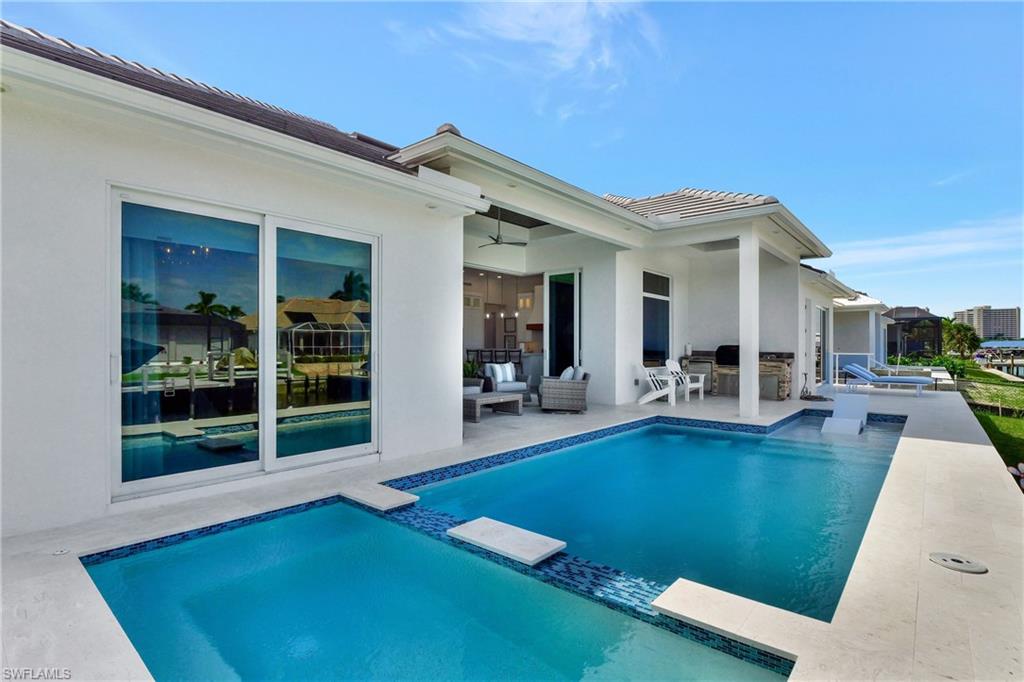 Expansive exterior featuring a tiled swimming pool, integrated spa, and a covered patio with an outdoor kitchen
