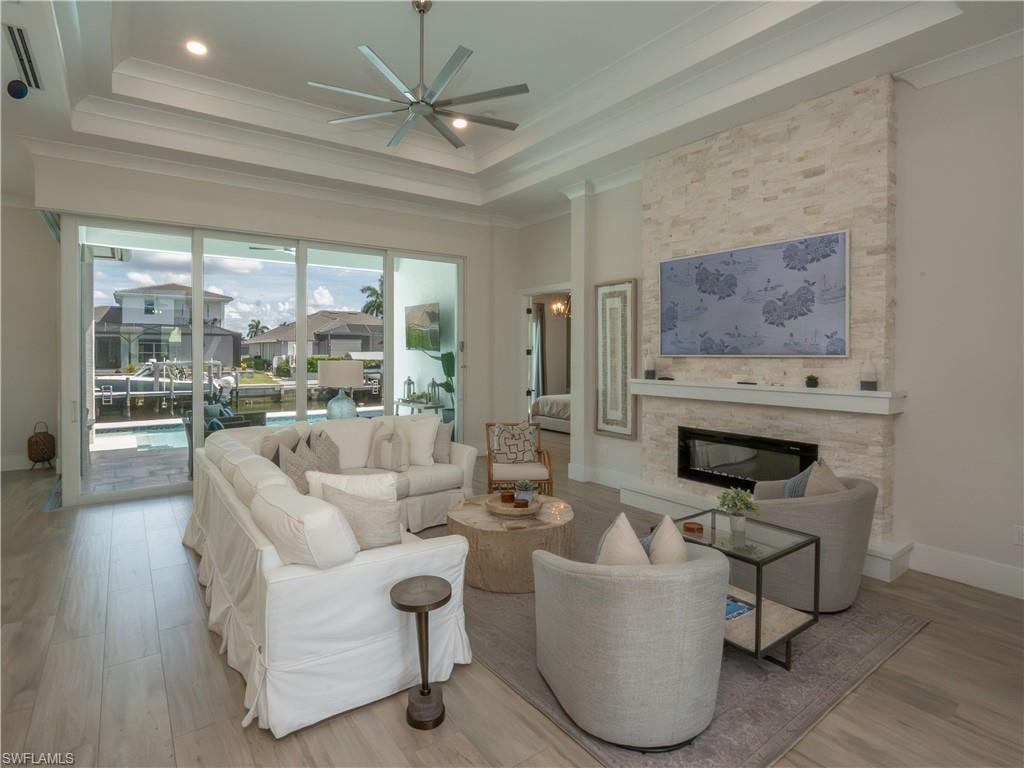Bright, open living room featuring a linear gas fireplace with stone surround, recessed ceiling with integrated ceiling fan, wide sliding glass doors opening to outdoor space, wood-finish flooring throughout, and a wall-mounted flat-screen television