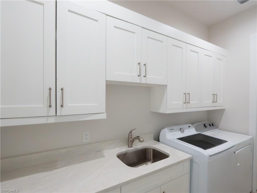 Modern laundry room featuring white shaker-style cabinetry with stainless steel hardware, quartz countertops, a stainless steel single-basin sink with chrome faucet, and a full-size front-load washing machine