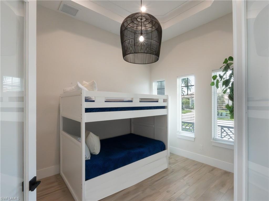 Bright bedroom featuring a white bunk bed with navy bedding, wood-finish flooring, and a black metal pendant light fixture