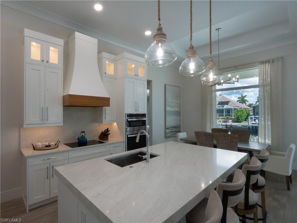 Modern kitchen featuring white cabinetry, a quartz waterfall-edge island countertop, stainless steel built-in appliances, pendant lighting with brass accents, and expansive windows overlooking outdoor spaces