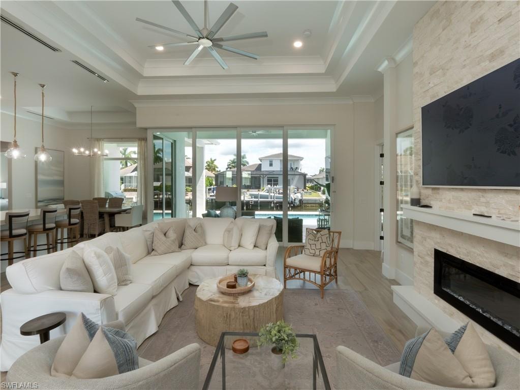 Tray ceiling with recessed lighting, wood-finish flooring, linear fireplace with stacked stone surround, sliding glass doors, and a ceiling fan