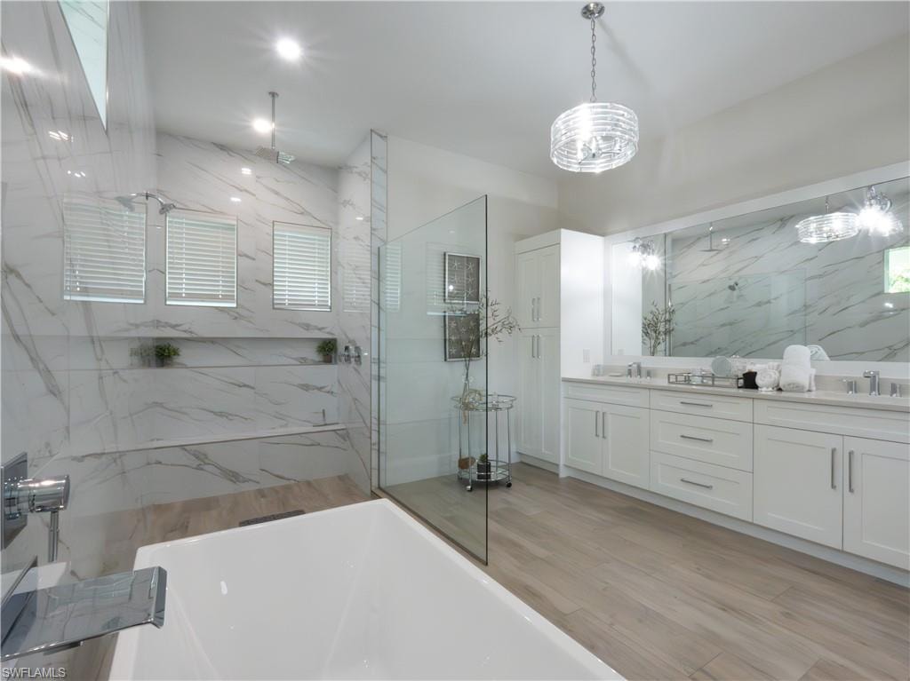 Freestanding bathtub, glass-enclosed shower with multiple showerheads, dual vanity with undermount sinks, and stone-look tile flooring