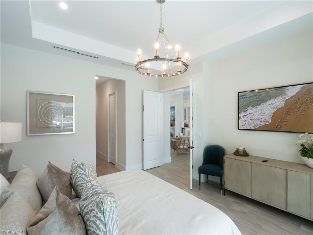Master bedroom featuring a wood-finish plank floor, soft neutral wall palette, and a decorative pendant light fixture with candle-style elements