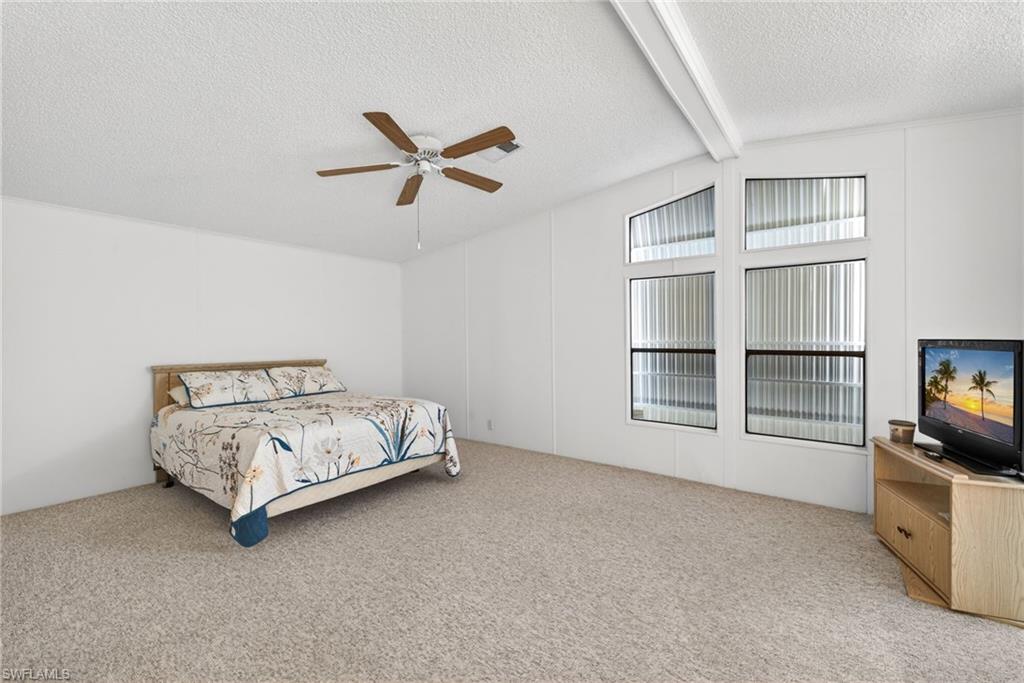 Spacious room featuring neutral carpeting, a ceiling fan with light fixture, and multiple windows with vertical blinds