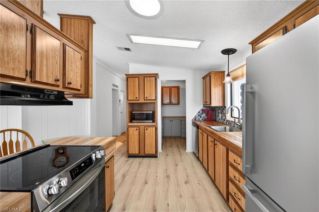 Kitchen featuring wood-finish cabinetry, wood-finish countertops, stainless steel appliances, and wood-finish flooring