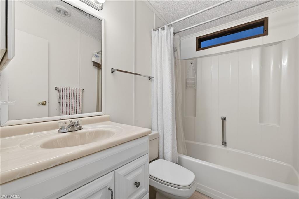 Bathroom featuring a white vanity with a tan countertop and integrated sink, a large wall mirror, a full bathtub with a shower surround, a toilet, and a transom window above the shower