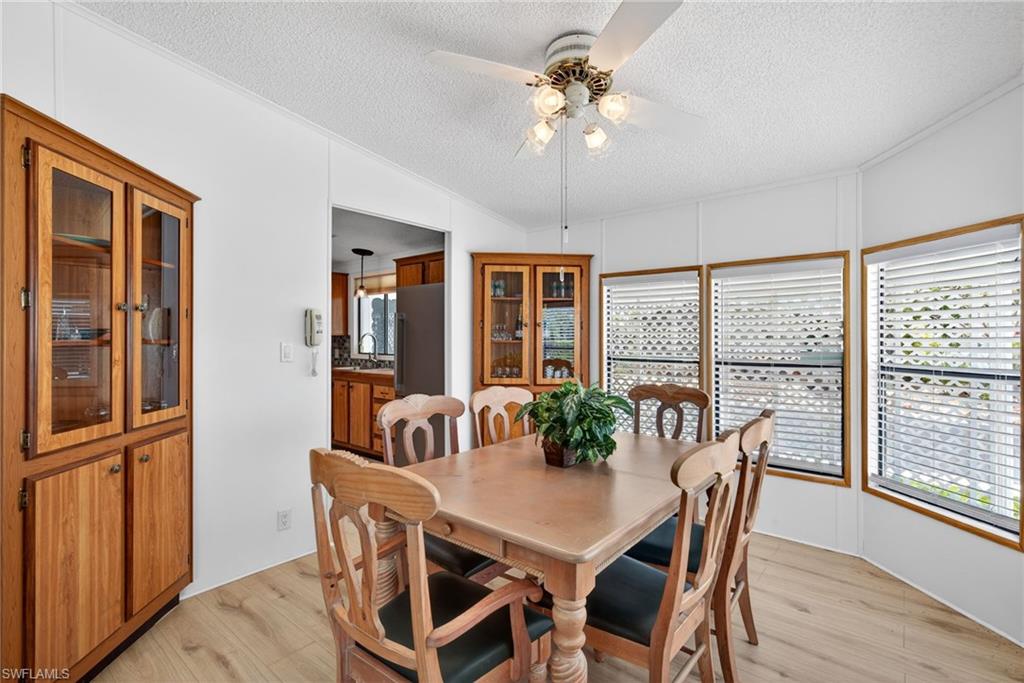 Dining area featuring wood-finish flooring, white paneling, multiple windows with blinds, and a ceiling fan with integrated lighting