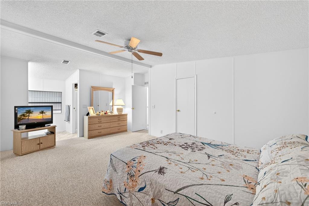 Spacious bedroom featuring neutral carpeting, a ceiling fan with light fixture, and white painted walls