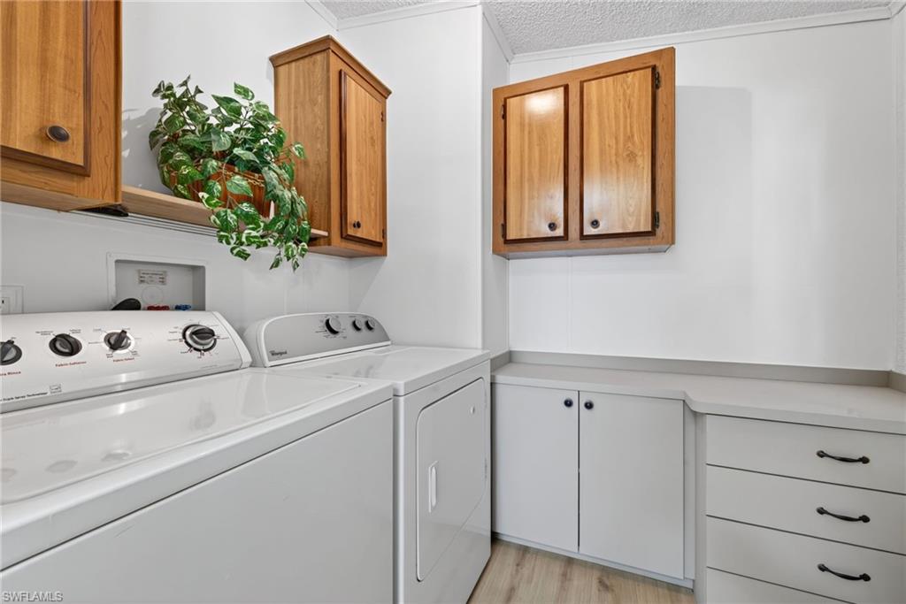 Dedicated laundry area featuring a washer and dryer, wood-finish upper cabinetry, lower cabinetry with drawers, and light-toned countertops