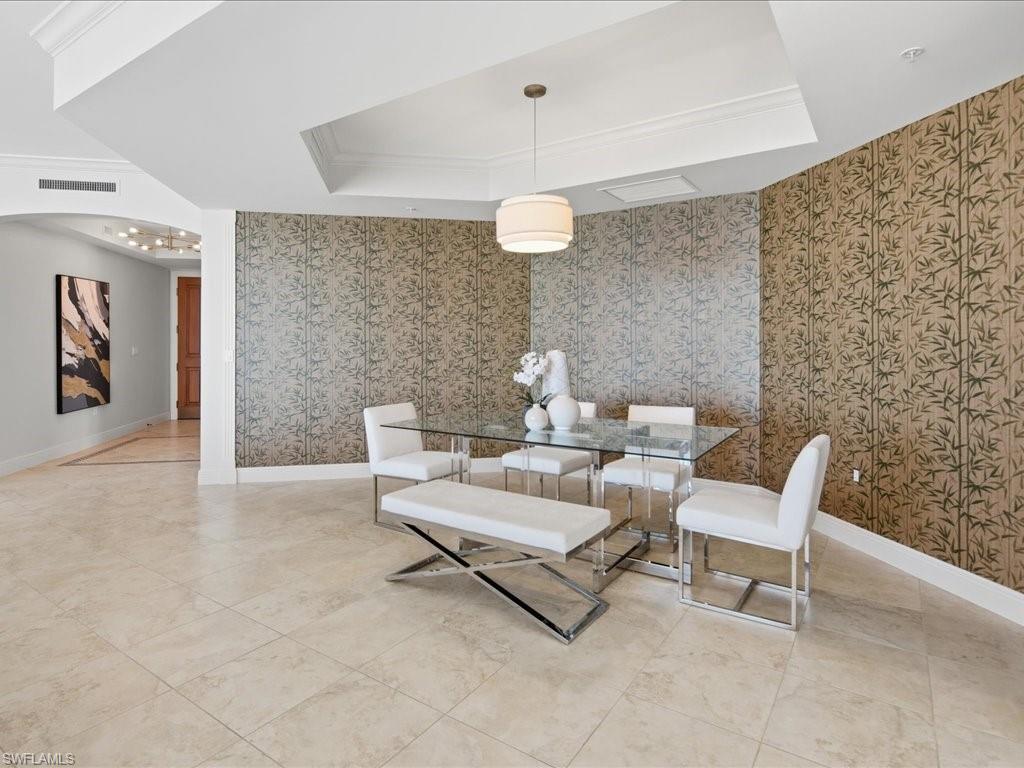 Dining area featuring textured wall coverings, tray ceiling with crown molding, and large format tile flooring