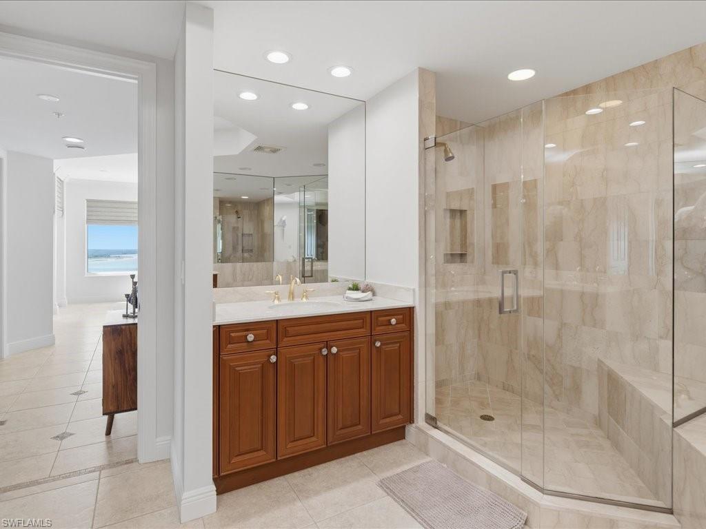 Spacious bathroom featuring a dual vanity with wood cabinetry and a large mirror, a glass-enclosed shower with a built-in bench, and recessed lighting