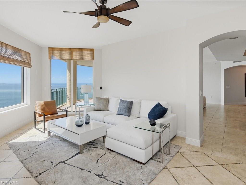 Spacious living area featuring large windows with natural light, a ceiling fan, and tile flooring with a decorative inlay