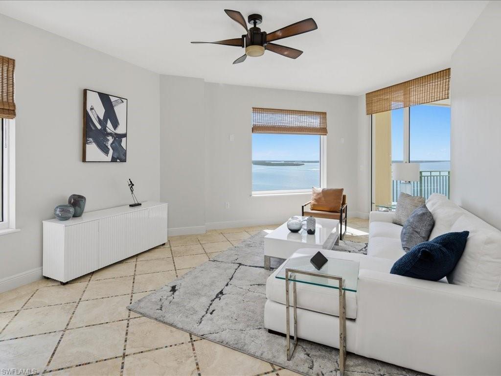 Expansive living area featuring large windows with water scenery, diagonally laid tile flooring, a modern ceiling fan, and a built-in console cabinet