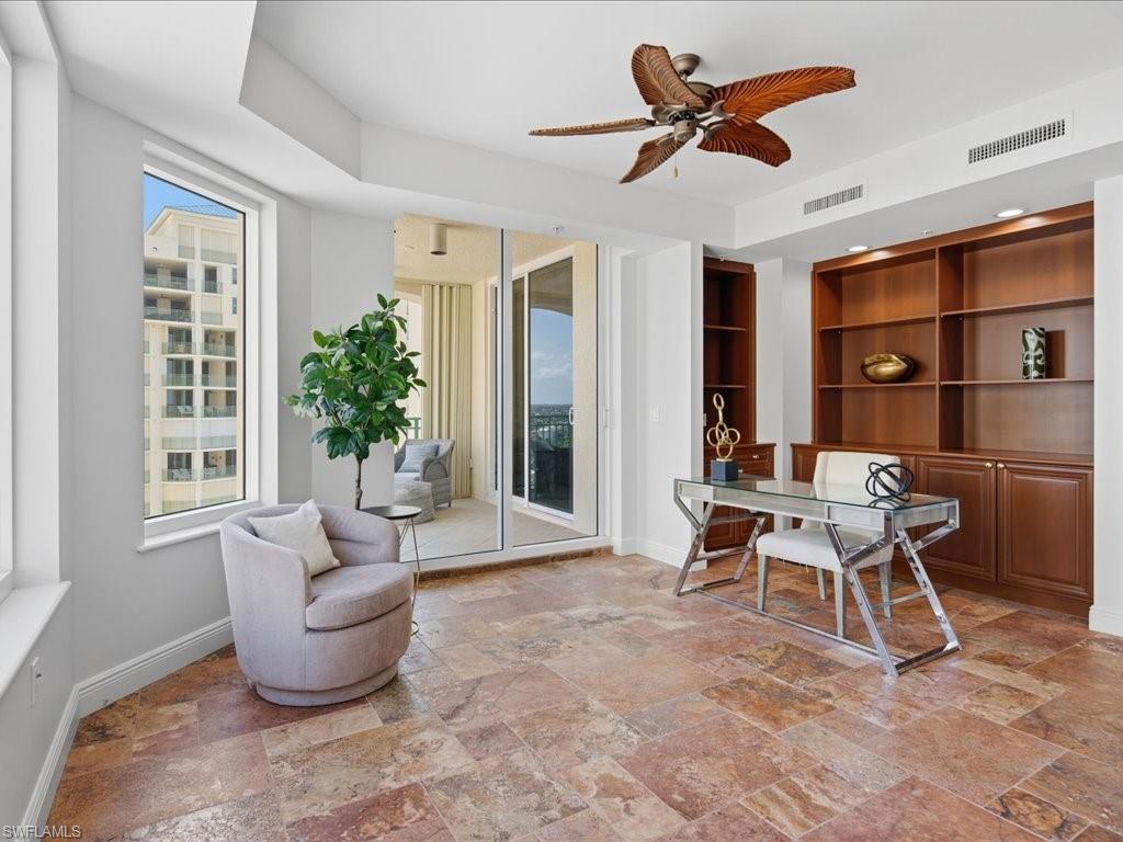 Office/3rd bedroom pacious room with large format stone tile flooring, a full wall of built-in wood cabinetry and shelving, a decorative ceiling fan, and sliding glass doors opening to a balcony