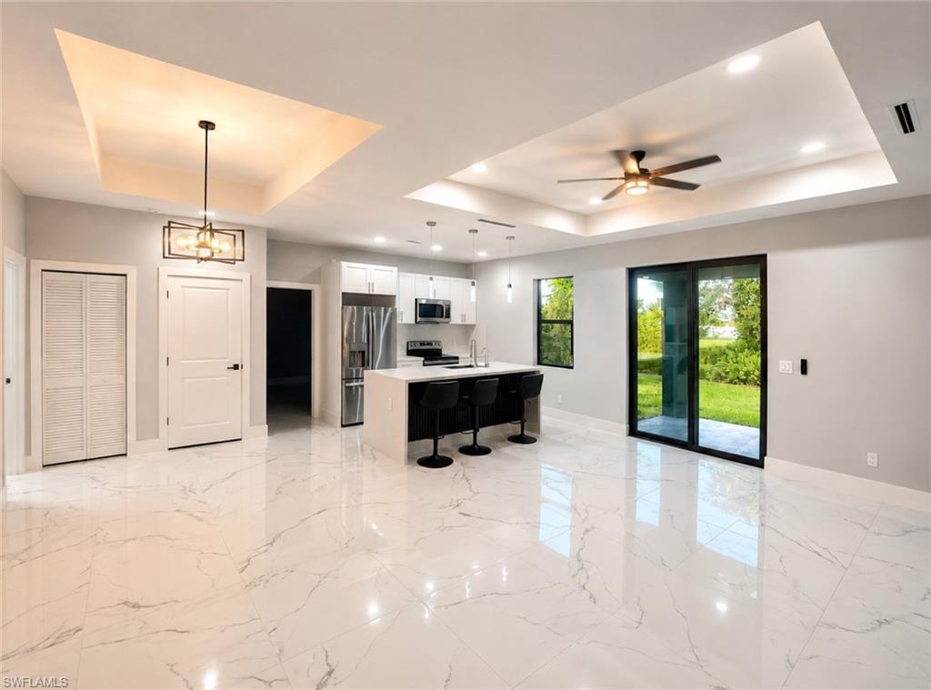 Open-concept living space with large format tile flooring and tray ceilings