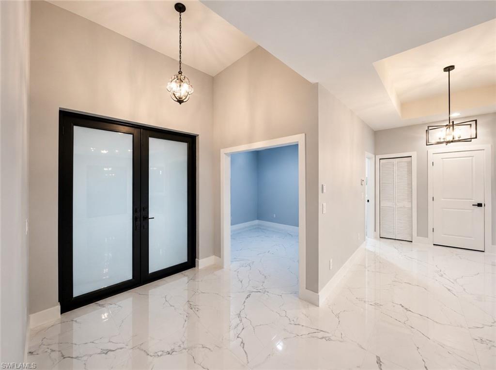 Spacious entryway featuring large format marble-look tile flooring, vaulted ceilings, and a modern chandelier