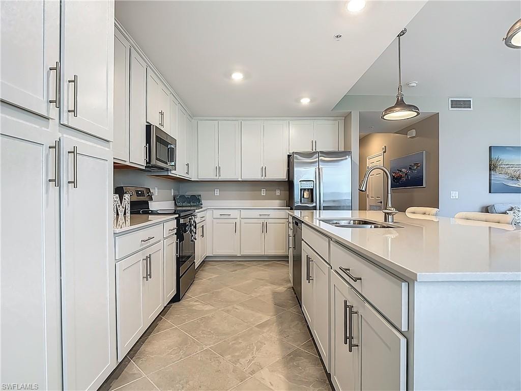 Kitchen featuring stainless steel appliances, light countertops, hanging light fixtures, white cabinets, and an island with sink