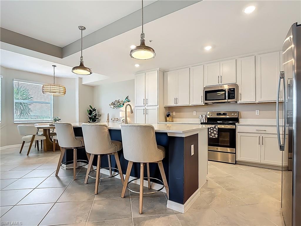 Kitchen featuring appliances with stainless steel finishes, a kitchen island with sink, light countertops, white cabinetry, and recessed lighting