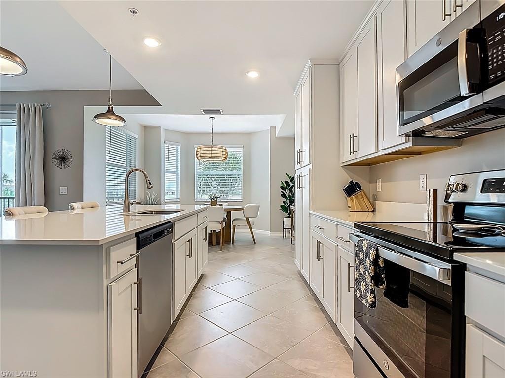 Kitchen with appliances with stainless steel finishes, light countertops, a center island with sink, decorative light fixtures, and recessed lighting
