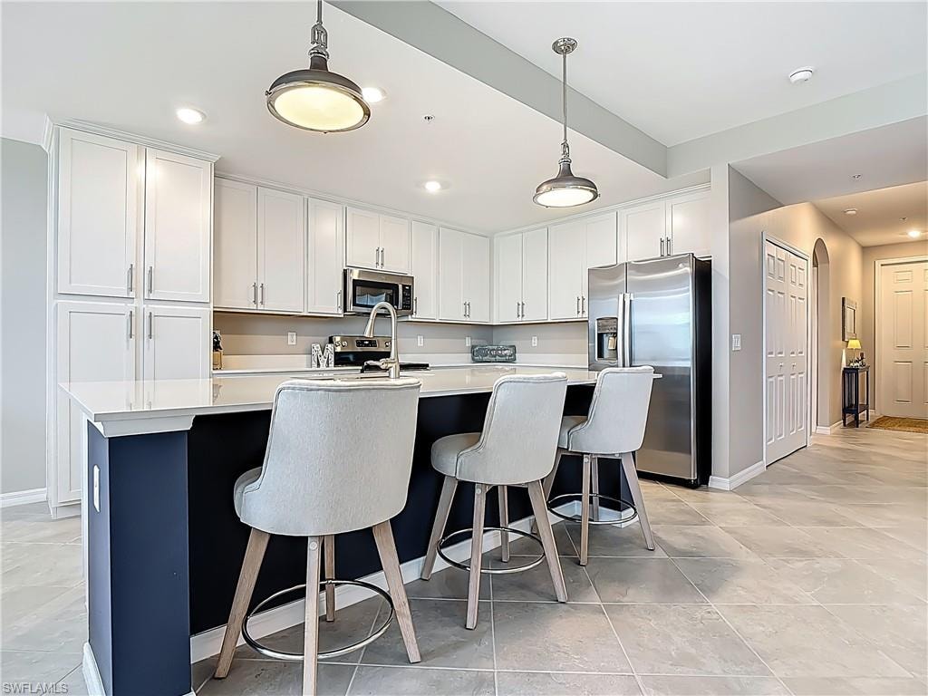Kitchen with stainless steel appliances, light countertops, a center island with sink, white cabinets, and hanging light fixtures