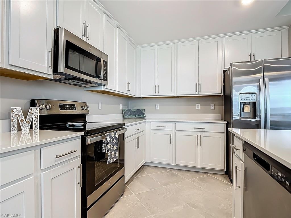Kitchen with stainless steel appliances, light countertops, white cabinets, and light tile patterned floors