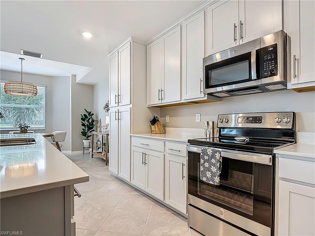 Kitchen with appliances with stainless steel finishes, light countertops, light tile patterned floors, white cabinets, and hanging light fixtures