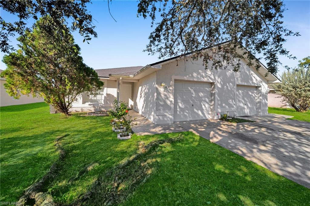 Exterior featuring a stucco finish, a two-car garage, a concrete driveway, and a front lawn with established landscaping