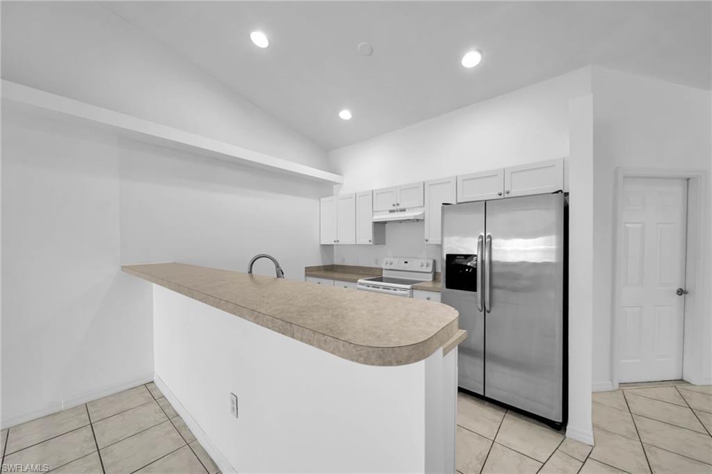 Kitchen featuring white shaker cabinetry, stainless steel appliances, a breakfast bar, and light-toned tile flooring