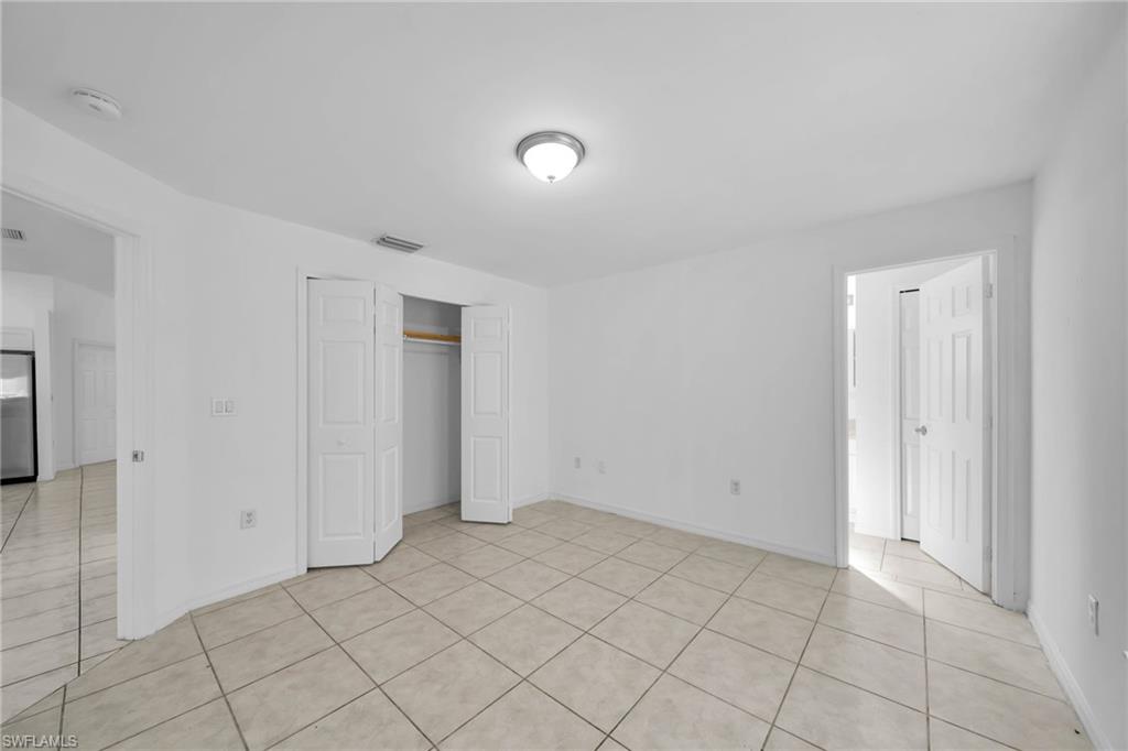 Spacious room featuring neutral tile flooring, white painted walls, a flush-mount ceiling light fixture, and a bi-fold closet with an interior hanging rod