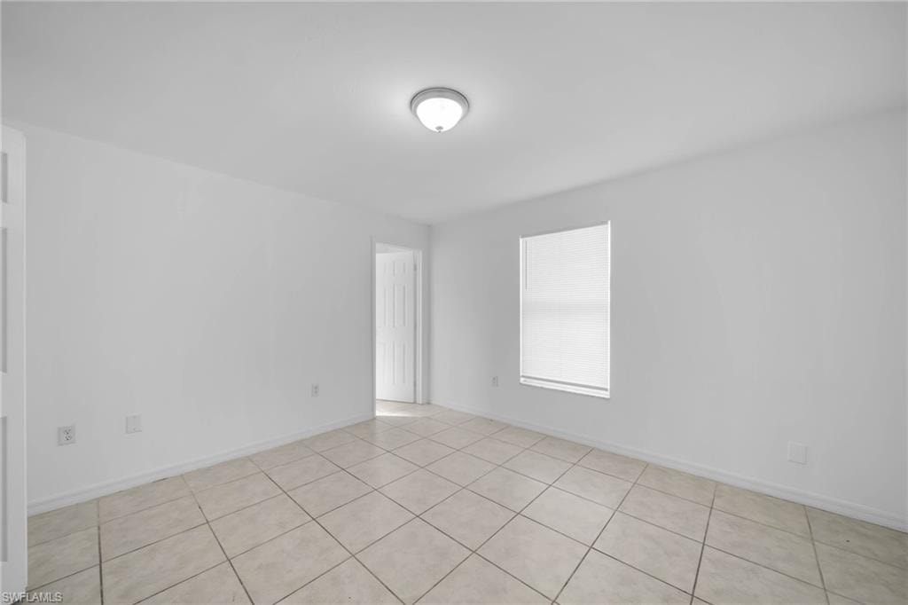 Bright interior space featuring light-colored tile flooring, white walls, and a window with blinds