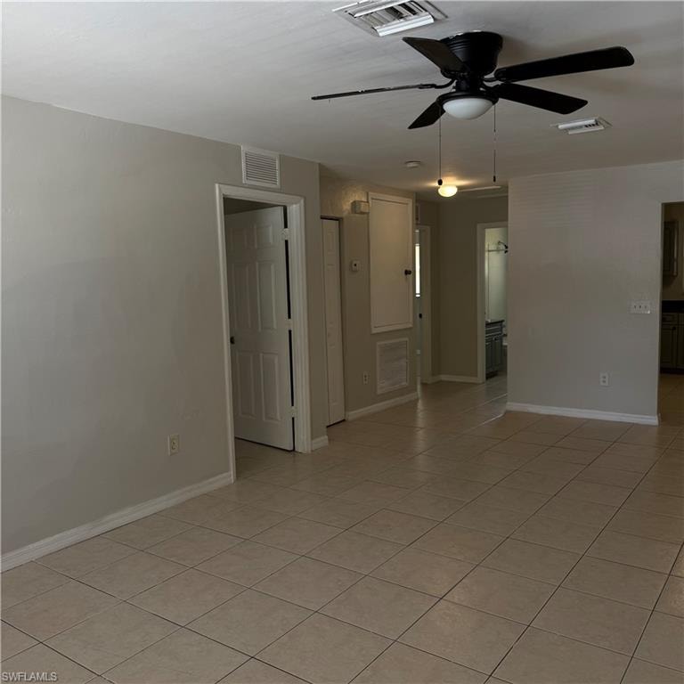 Spacious room featuring tile flooring, neutral wall tones, a ceiling fan with integrated lighting, and white trim molding