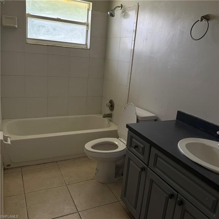 Bathroom featuring a white bathtub with white tile surround, a built-in shower fixture, a toilet, and a vanity with an integrated sink and dark countertop