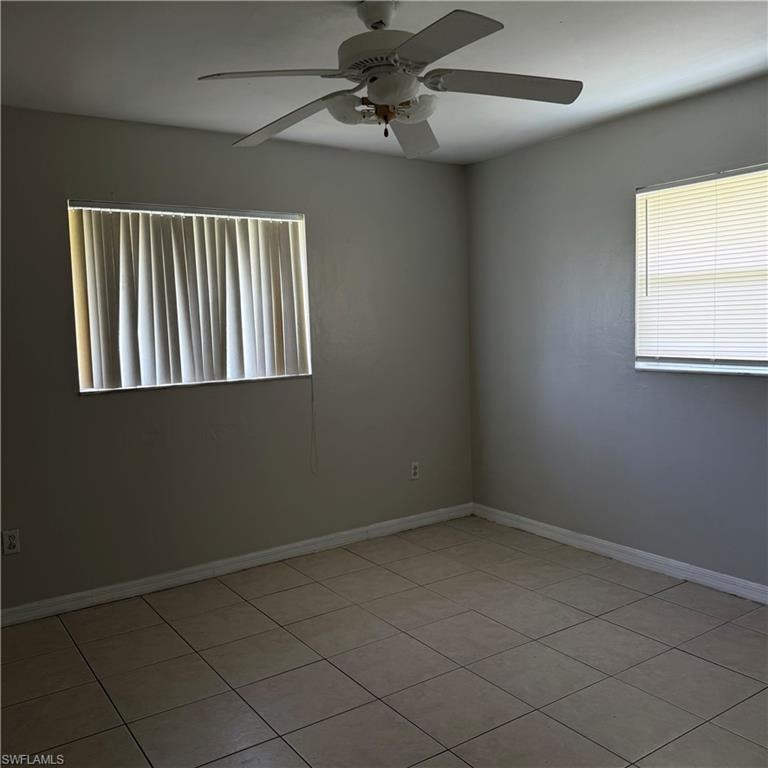 Tiled flooring throughout this room featuring a ceiling fan, two windows with blinds, and neutral painted walls
