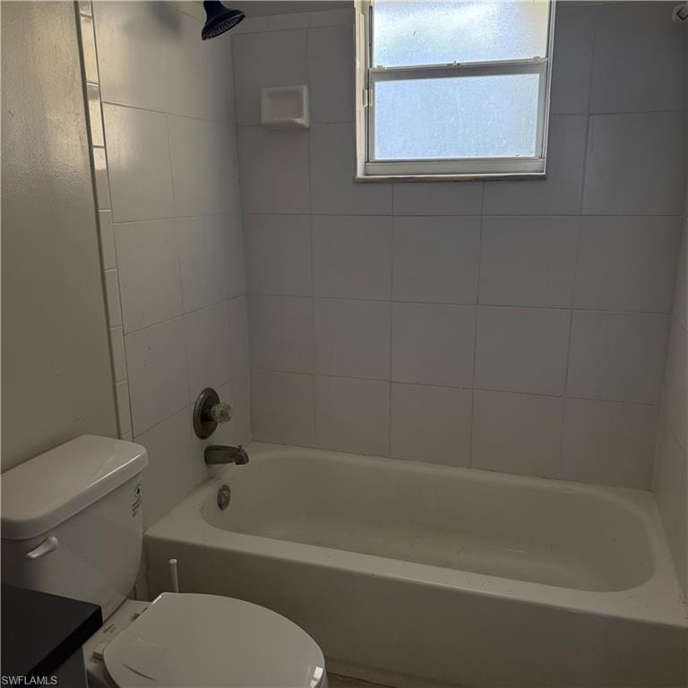 White tiled bathroom featuring a built-in bathtub, a window with frosted privacy glass, and a wall-mounted shower head