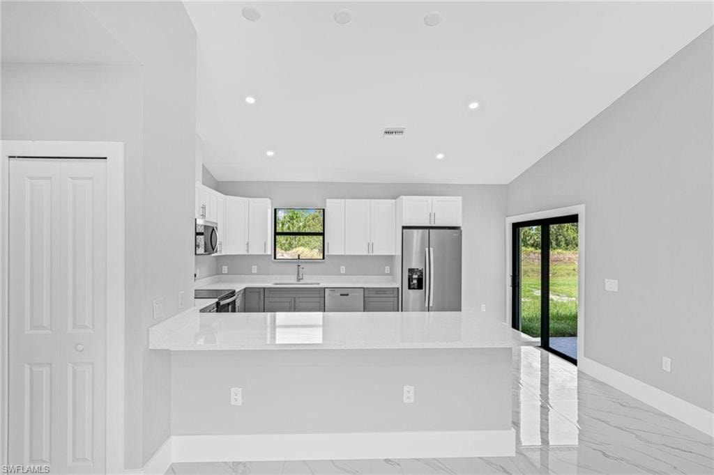 Kitchen featuring white upper cabinetry, gray lower cabinetry, stainless steel appliances, a breakfast bar, and vaulted ceilings