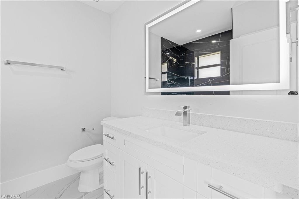 Black marble-finish wall with white veining, white bathtub, wall-mounted shower fixture, modern vanity with stone countertop, and illuminated mirror