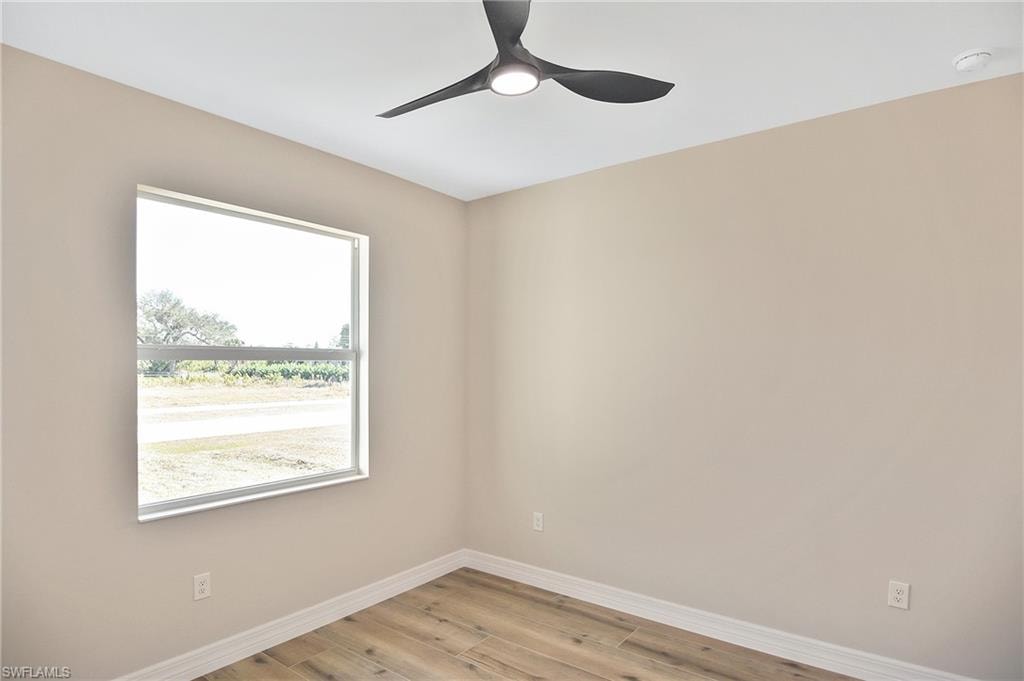 Bright interior space featuring a modern ceiling fan with integrated lighting, a large window, light neutral wall paint, white baseboards, and wood-finish flooring