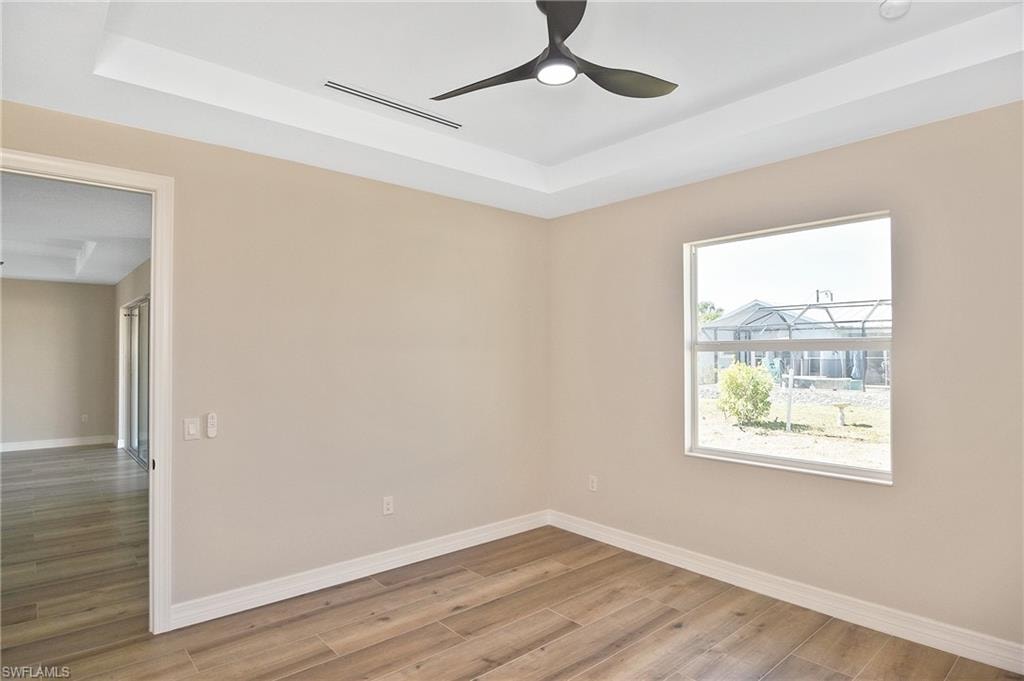 Spacious room featuring wood-finish flooring, a contemporary ceiling fan, and a tray ceiling