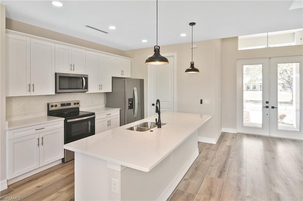 Kitchen featuring white shaker cabinetry, stainless steel appliances, and a central island with an undermount sink and two pendant lights