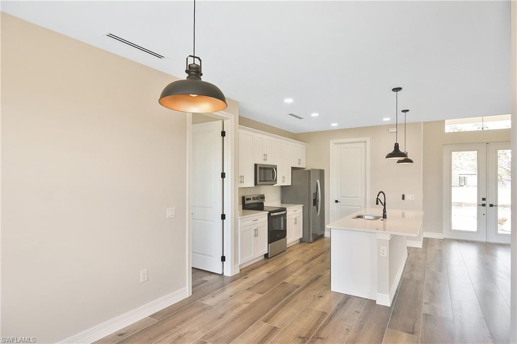 Open-concept kitchen featuring white cabinetry, stainless steel appliances, a center island with a sink and breakfast bar, and wood-finish flooring