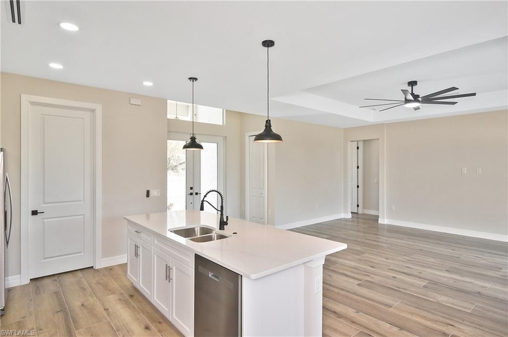 Open-concept kitchen and living area featuring a white quartz island with integrated sink and dishwasher, wood-finish flooring, and a tray ceiling with a modern ceiling fan