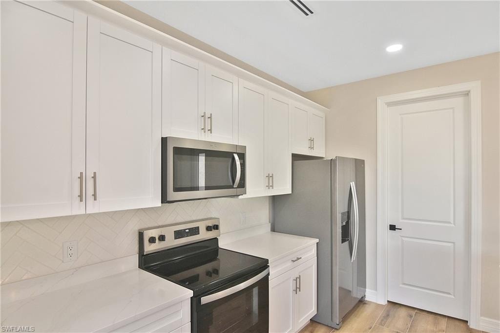 Kitchen featuring white shaker cabinetry, stainless steel appliances, light-toned countertops, a herringbone tile backsplash, and wood-finish flooring